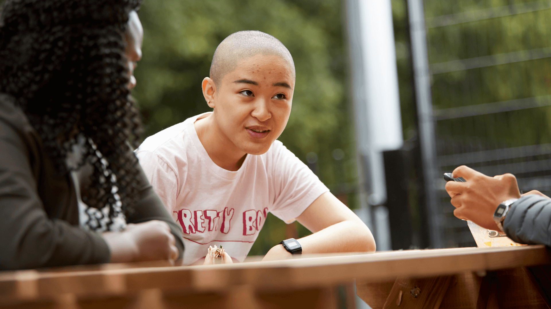a-young-woman-with-shaved-head-talking-to-her-friends-while-sitting-on-a-dining-bench-in-a-park