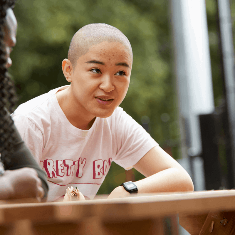 a-young-woman-with-shaved-head-talking-to-her-friends-while-sitting-on-a-dining-bench-in-a-park