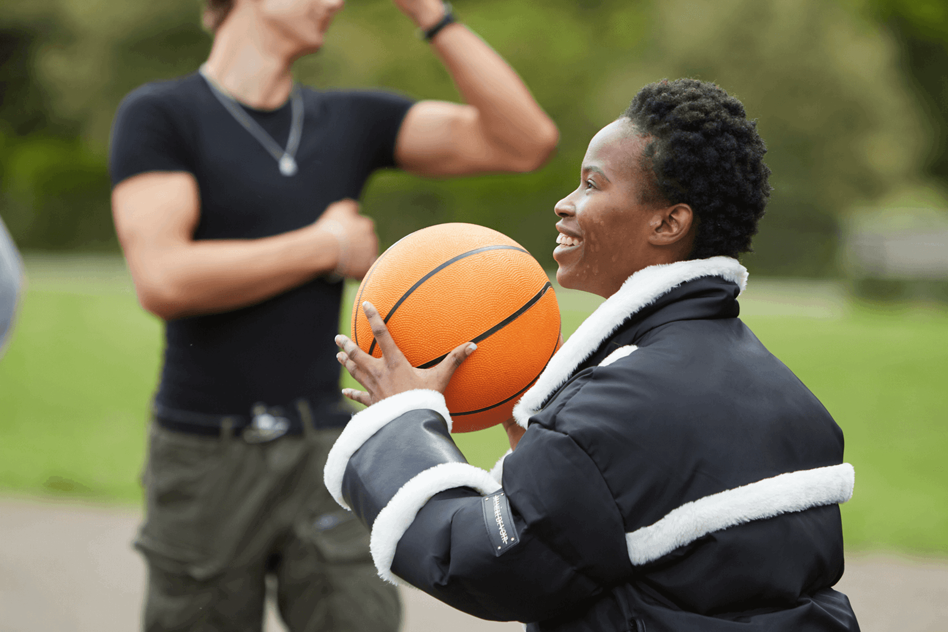 medium shot of a girl with short curly hair wearing black jacket and holding a basketball while smiling and playing with boys