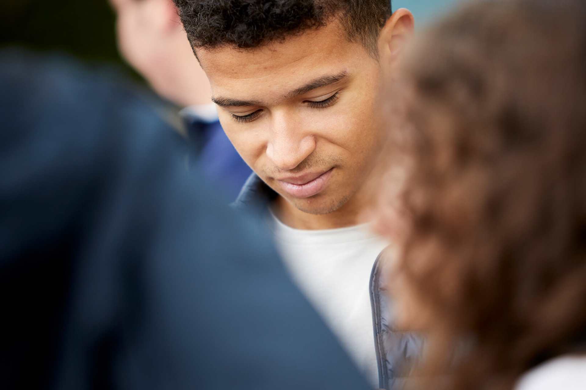 A young man stands in the centre of a group of friends with his eyes and head down.