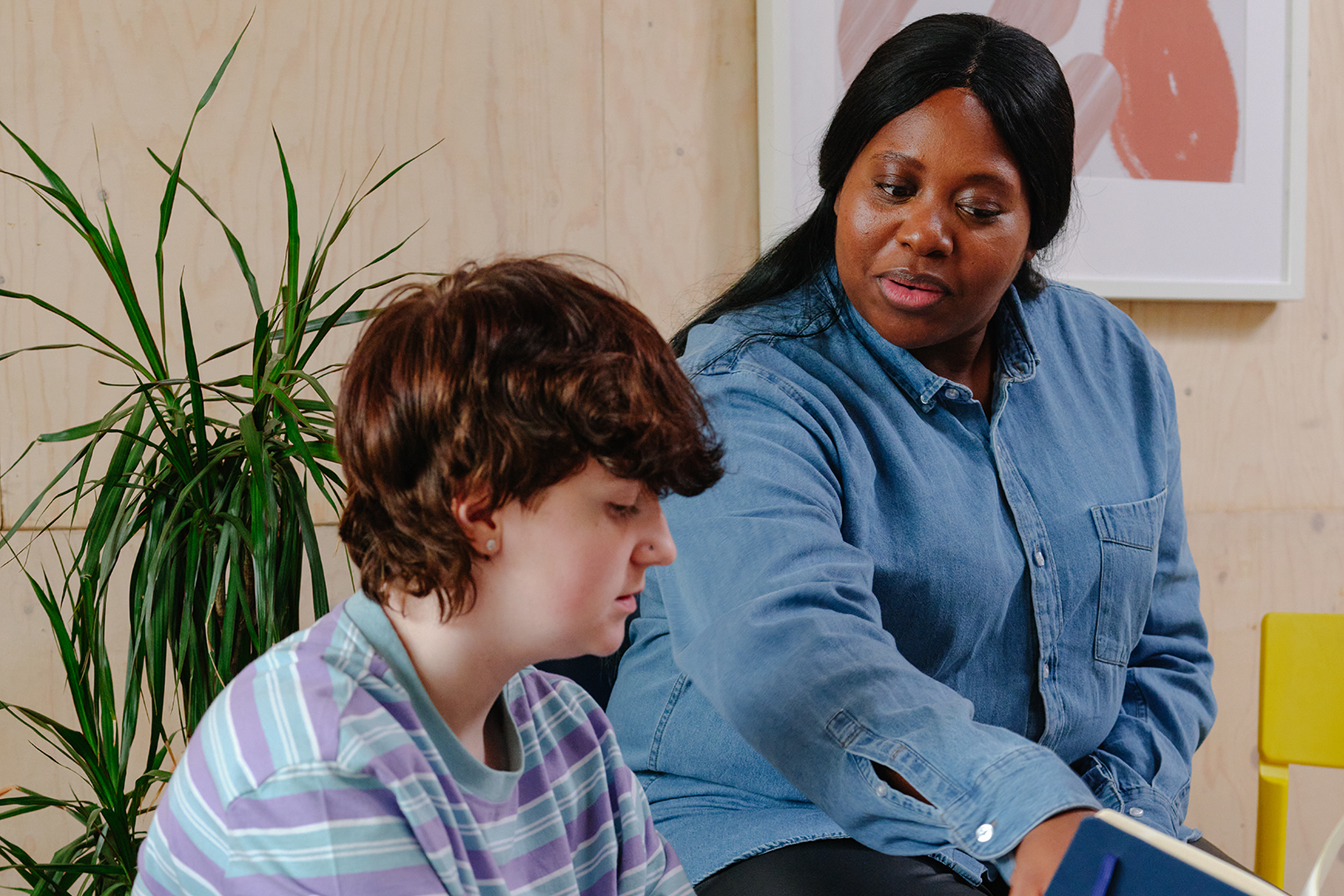 A white non-binary teenager reading with an older Black woman in a professional setting.