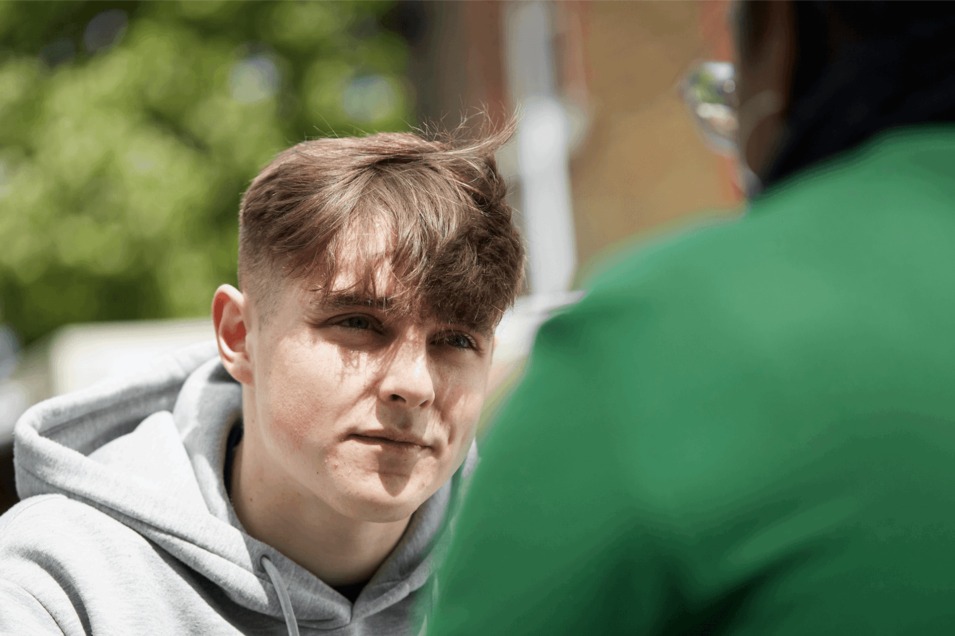 close up of a boy wearing grey hoodie listening to an advice of his teacher in front of him
