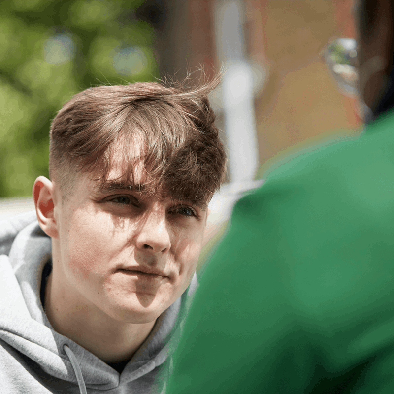 close up of a boy wearing grey hoodie listening to an advice of his teacher in front of him