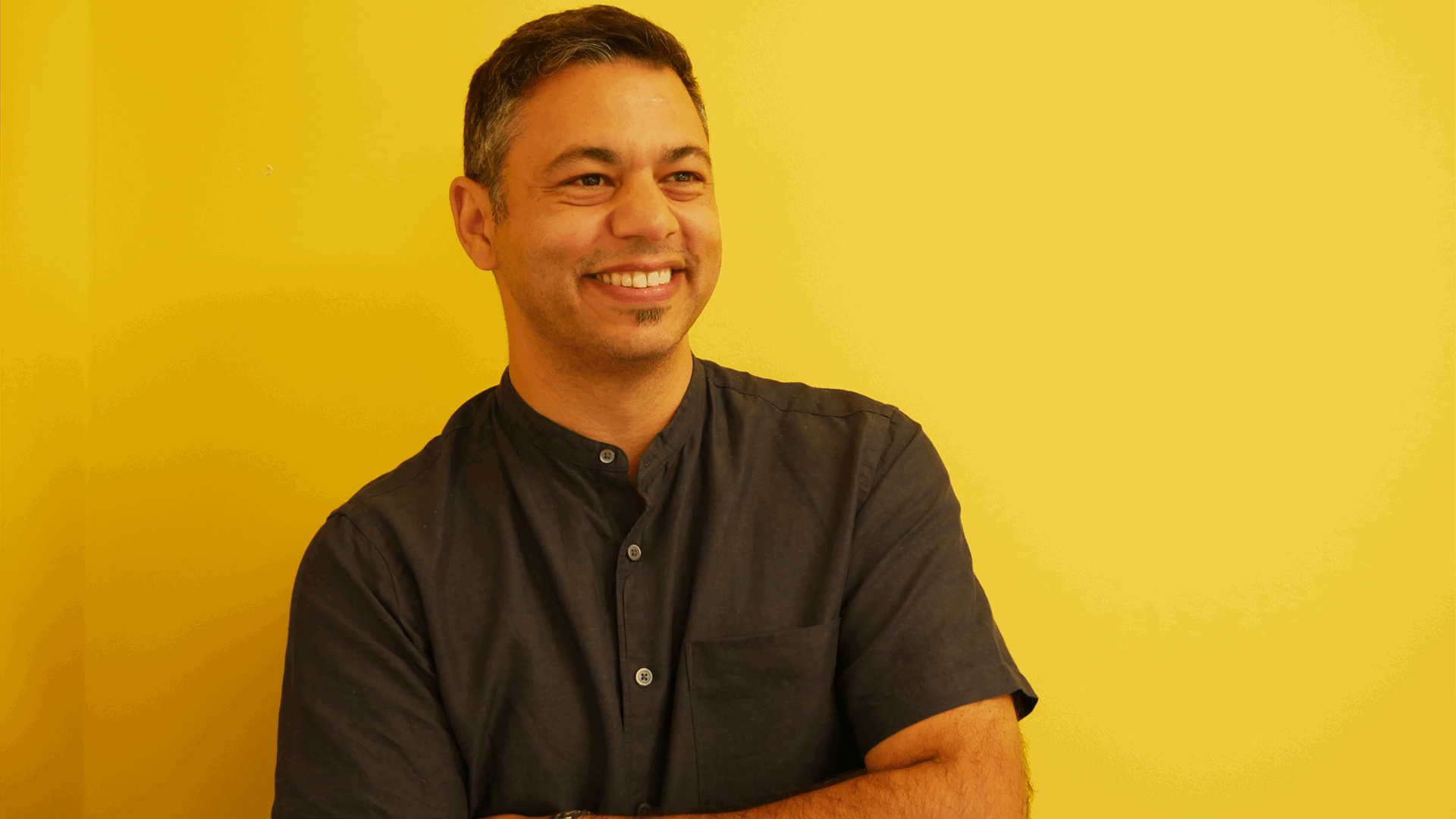 YoungMinds staff member Sacha Dingomal smiling against a yellow background