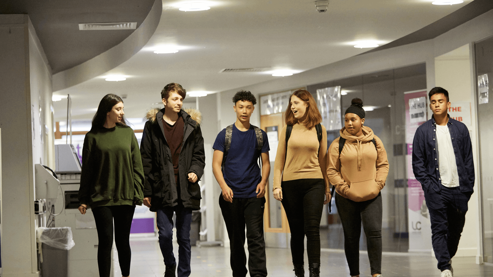 wide shot of six students walking and talking while walking in the hallway of the campus