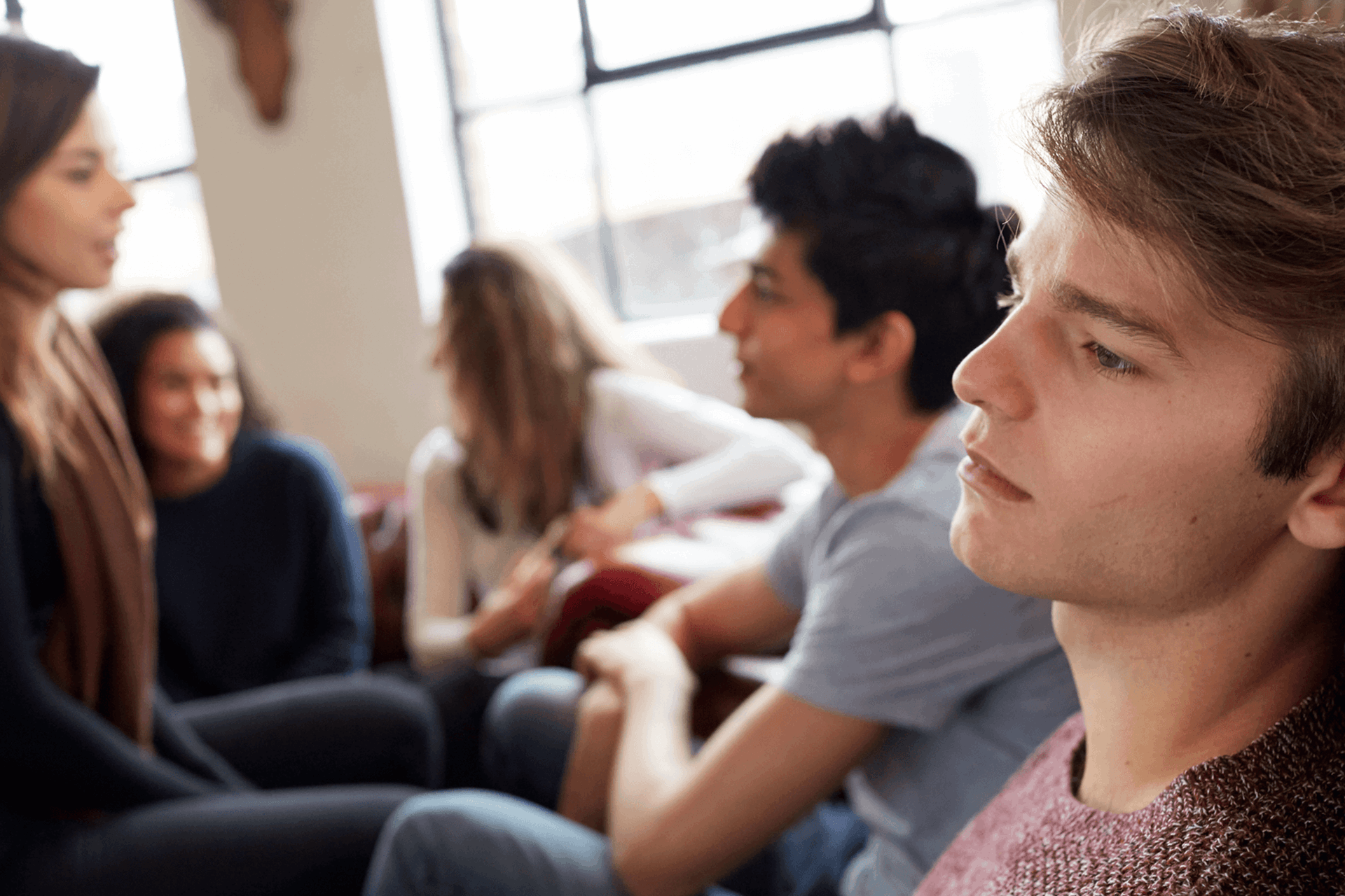 A young person lost in thought while sitting with their group of friends who are talking together.