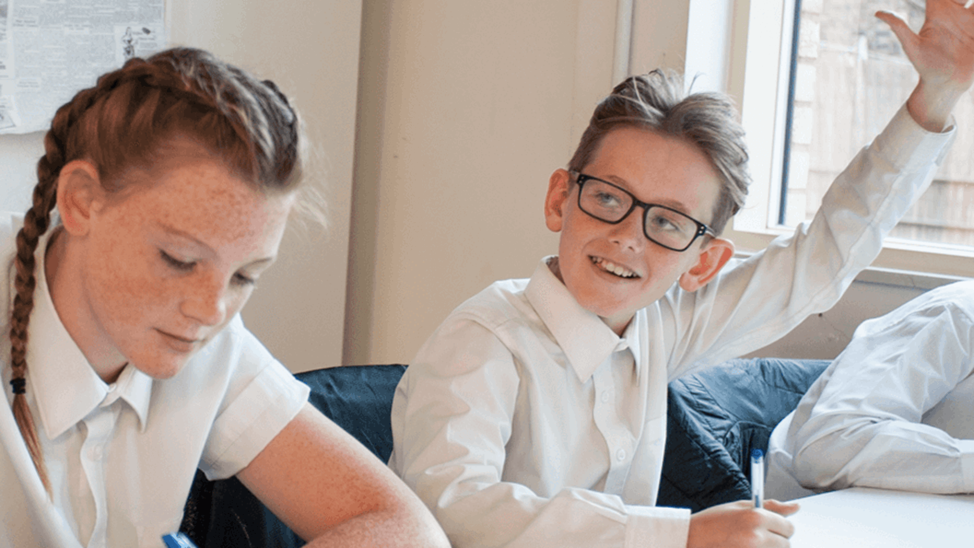 A male teacher sitting with his students at their desk smiling