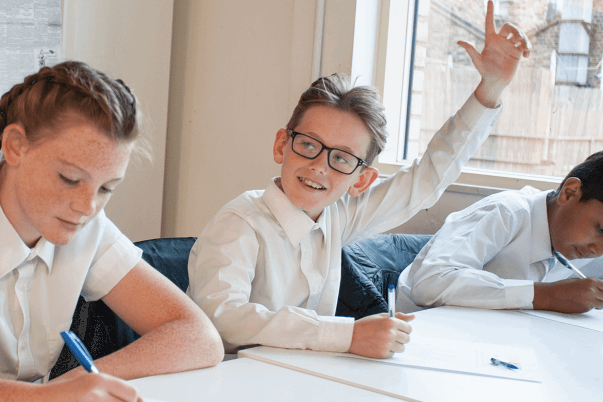 A male teacher sitting with his students at their desk smiling