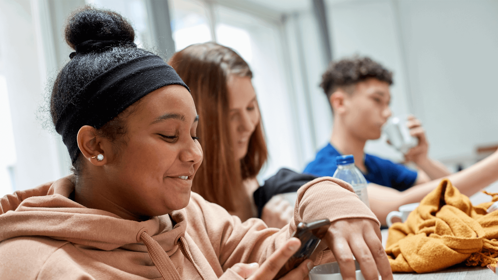medium-shot-of-three-young-people-smiling-while-looking-at-their-phone-while-sitting-in-class