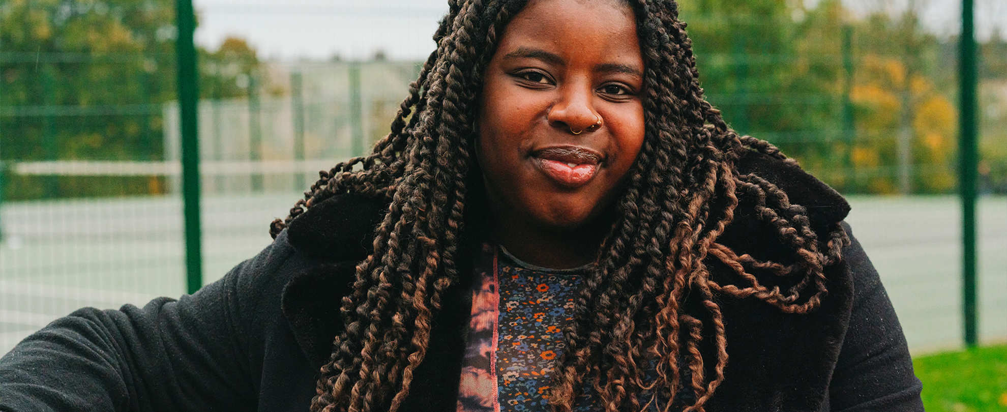A young Black woman sitting on a bench in the park. She is smiling.