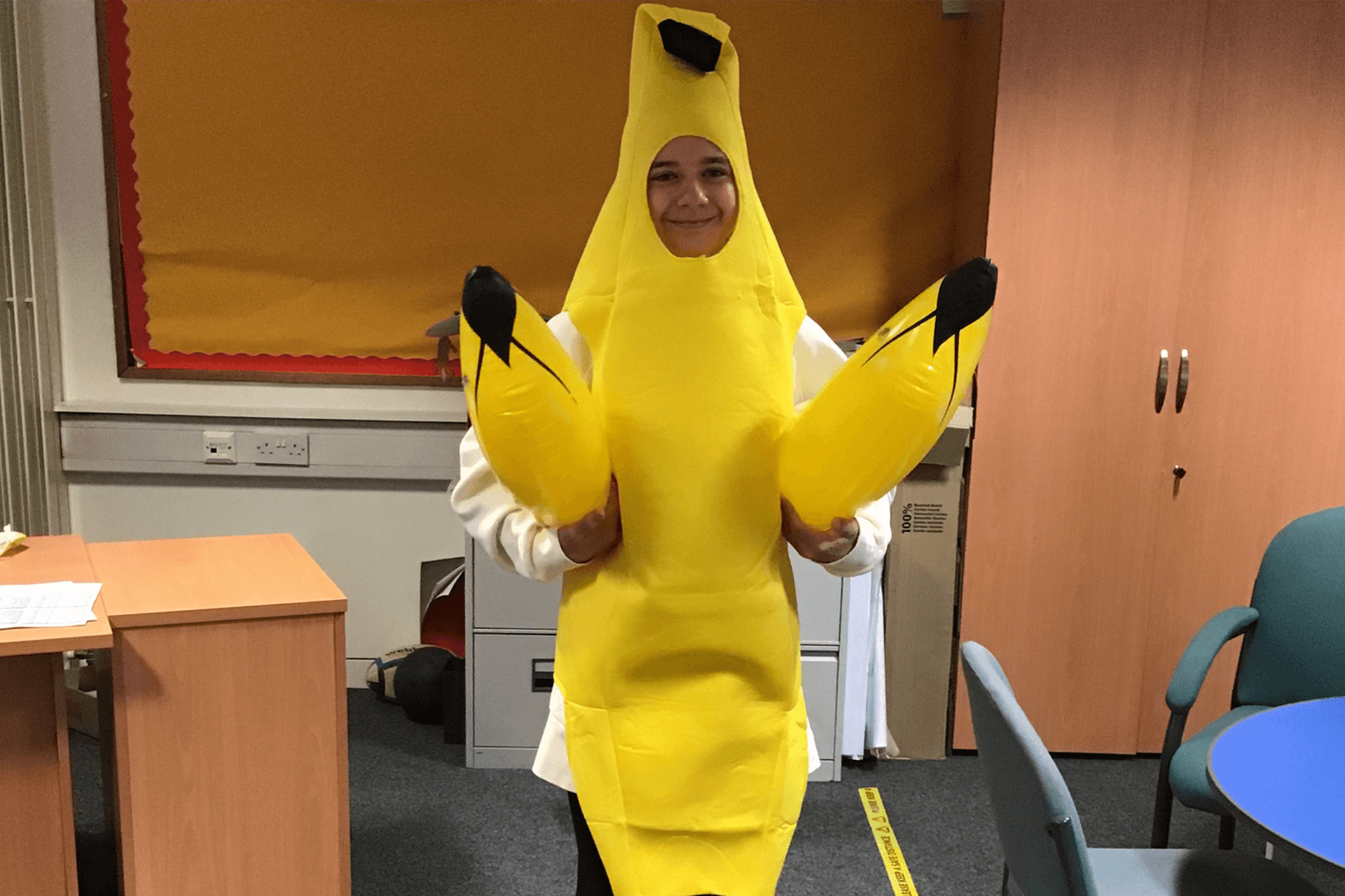 A person stands wearing a banana costume hold two inflatable bananas