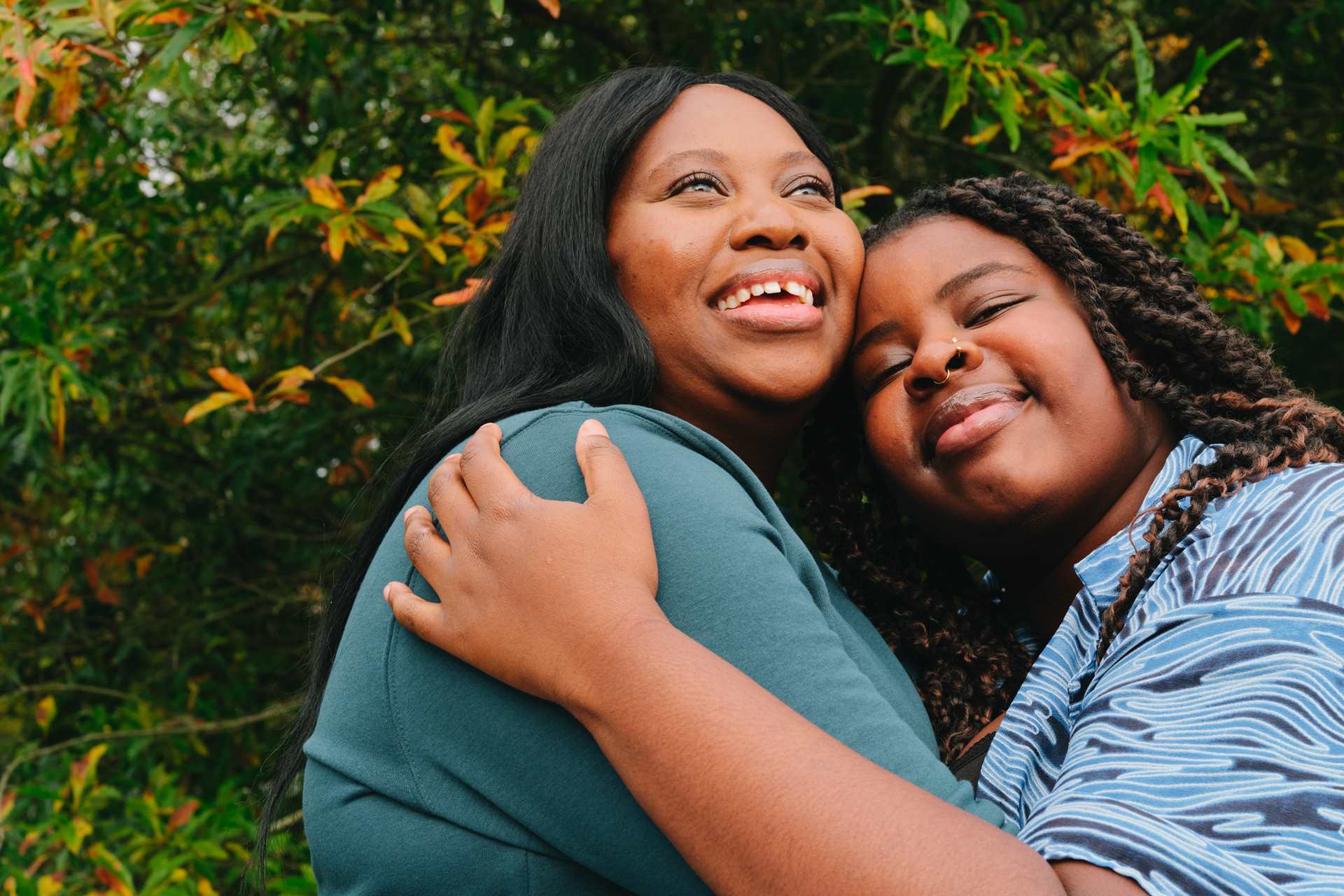 A young Black woman hugging an older Black woman in the park on a bench. They are both smiling.