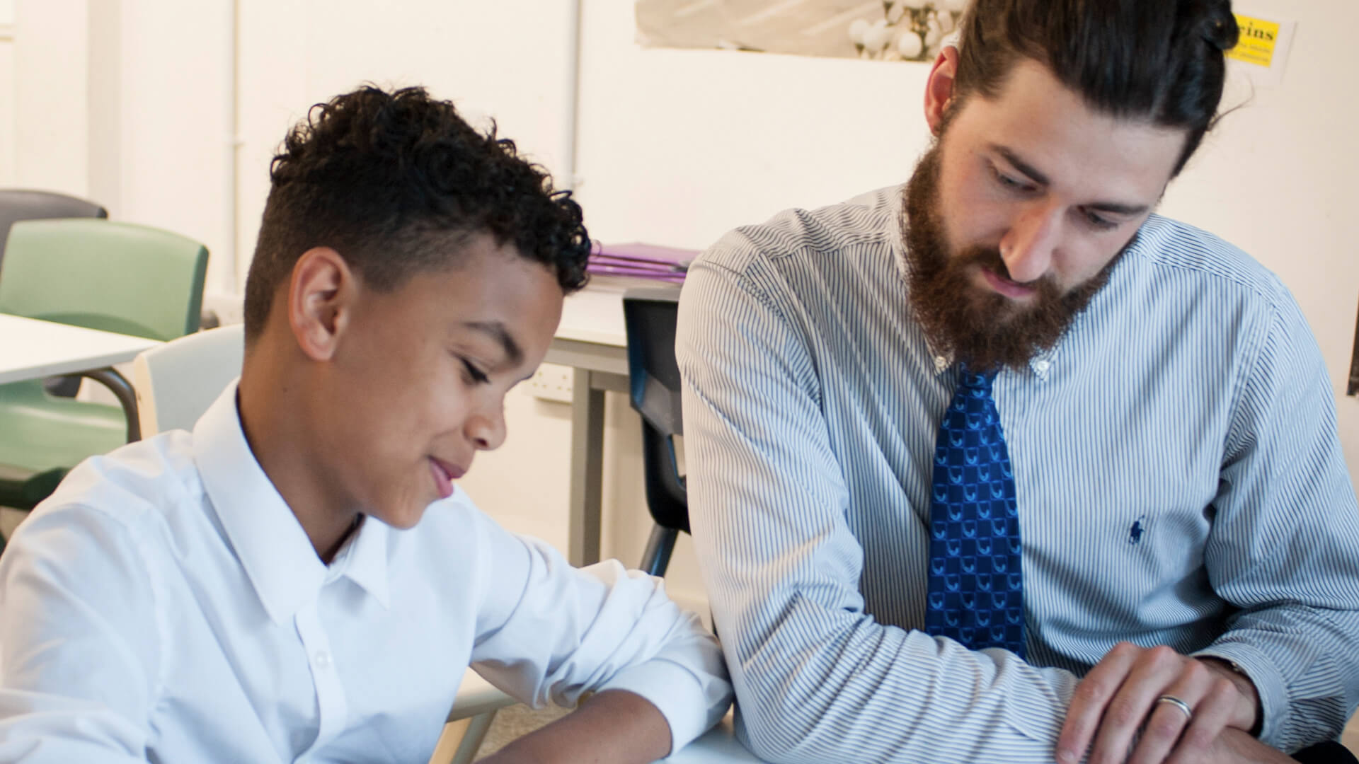 a teacher sits beside a student to help him read his lesson on his desk inside the classroom