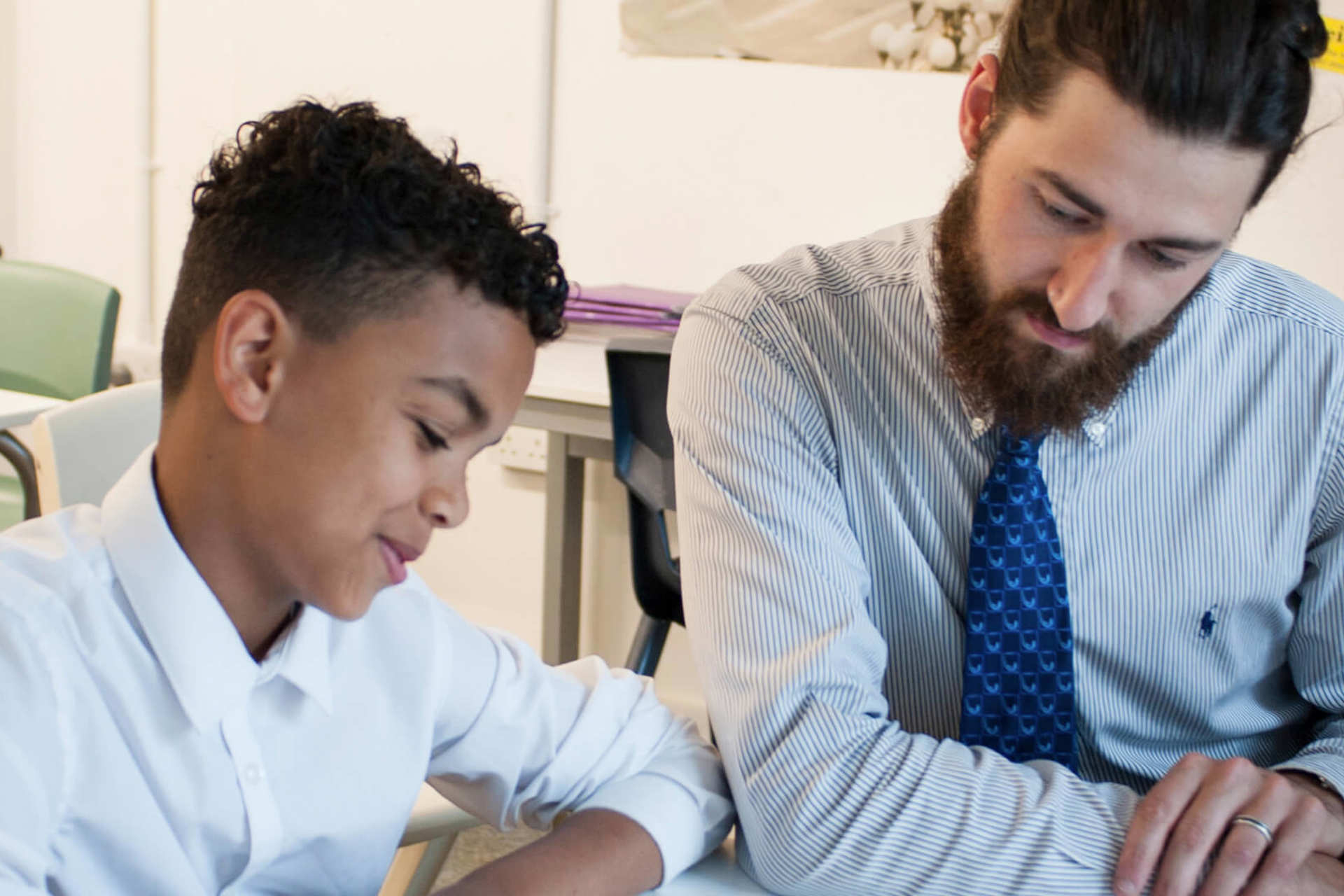 a teacher sits beside a student to help him read his lesson on his desk inside the classroom
