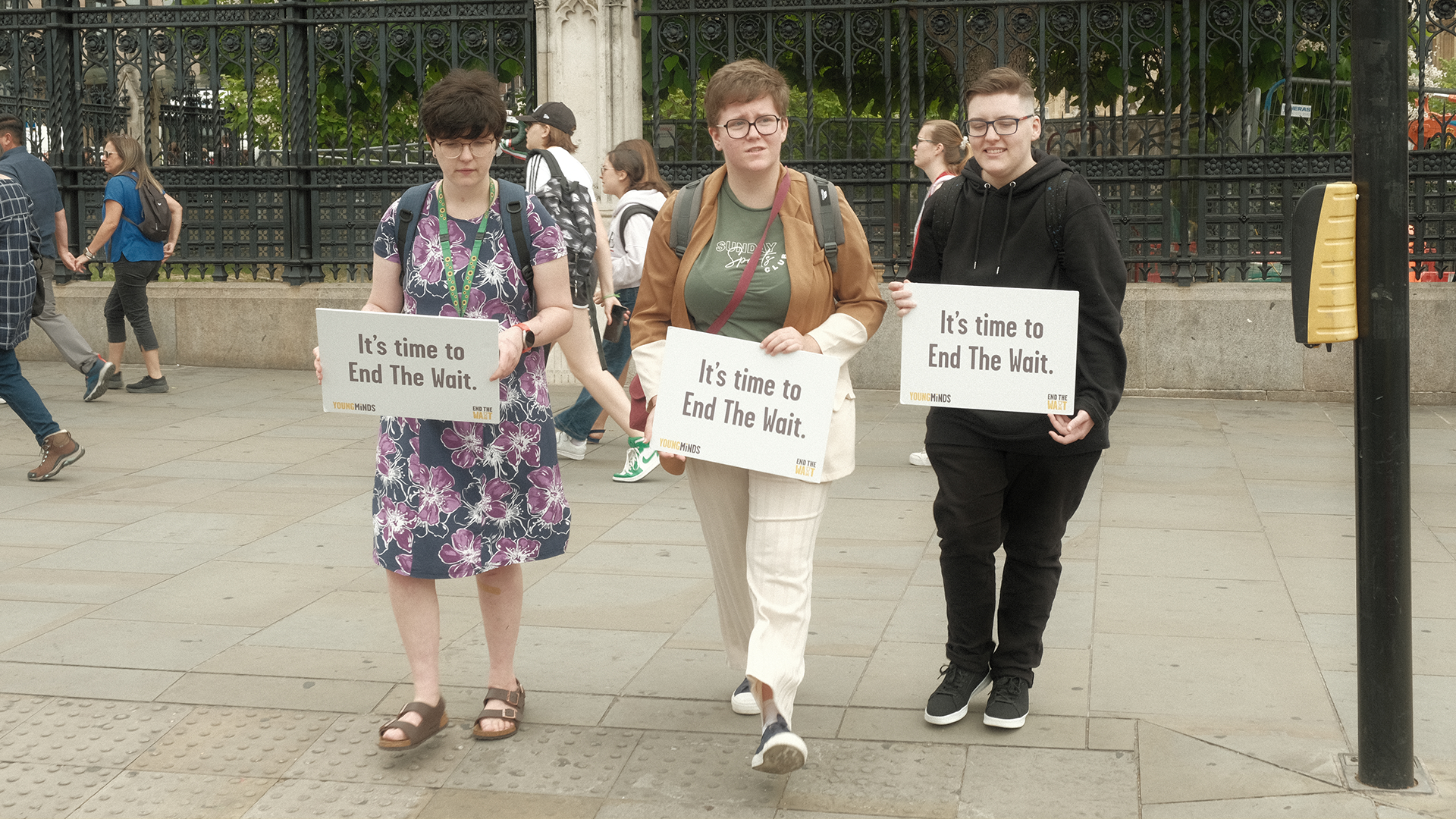 Three Activists holding signs in Parliament Square that read: "It's time to End The Wait."