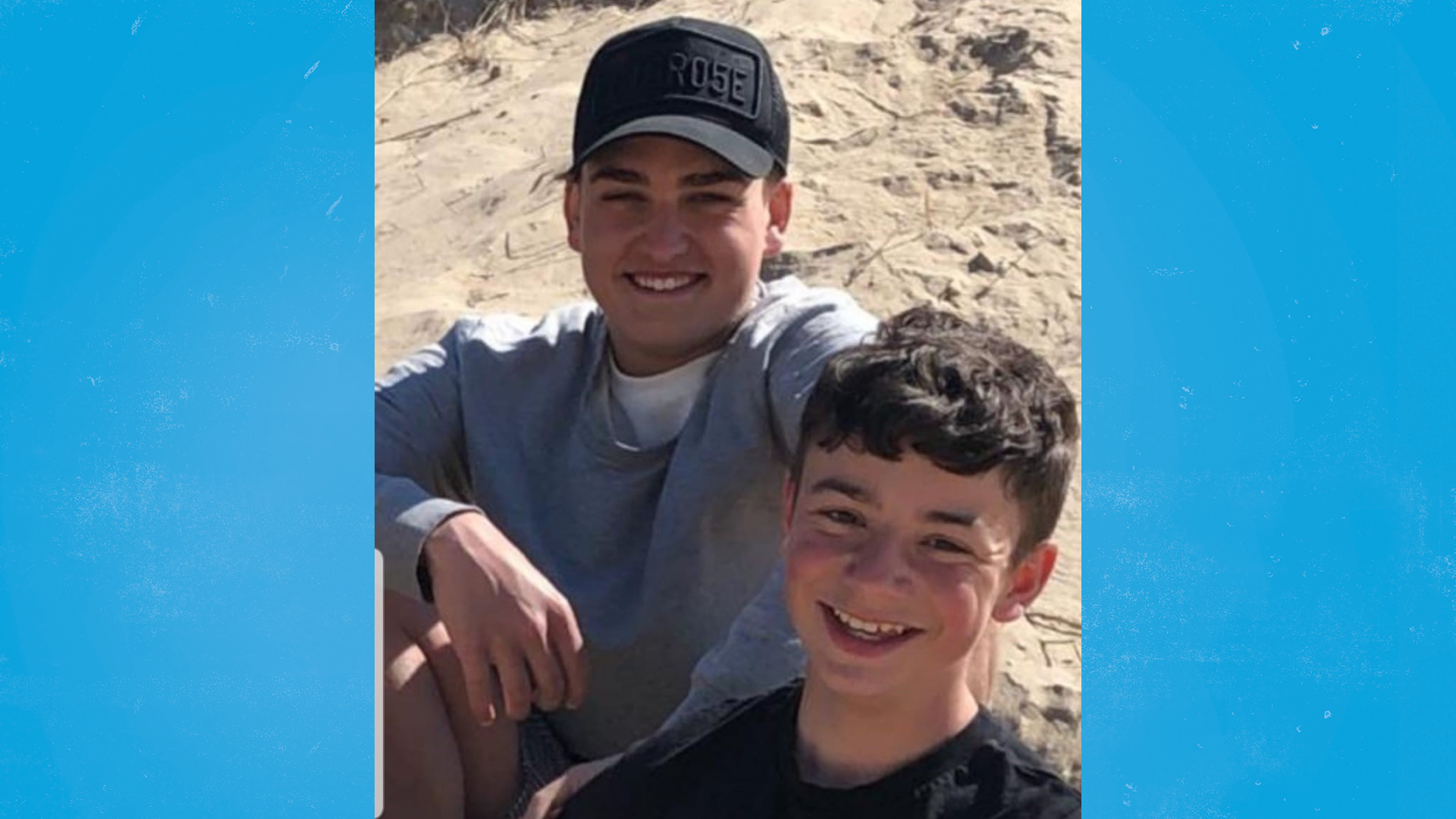 A photo of Riley and Trey, smiling while sat on the beach.