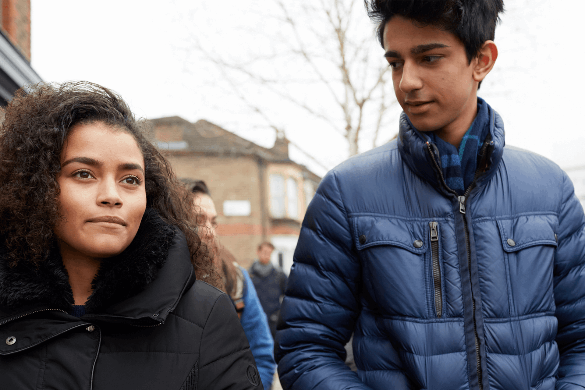 Two young people wearing coats and walking together down a street.