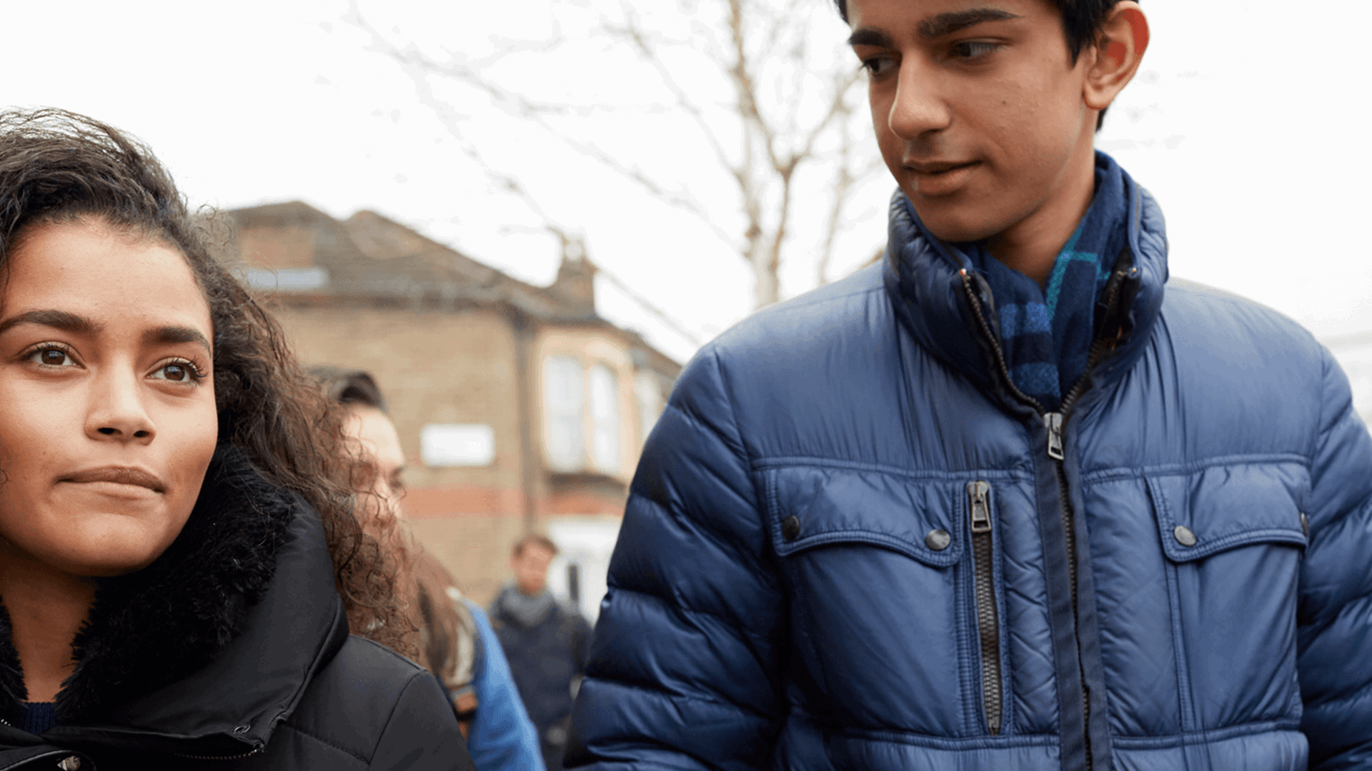 Two young people wearing coats and walking together down a street.