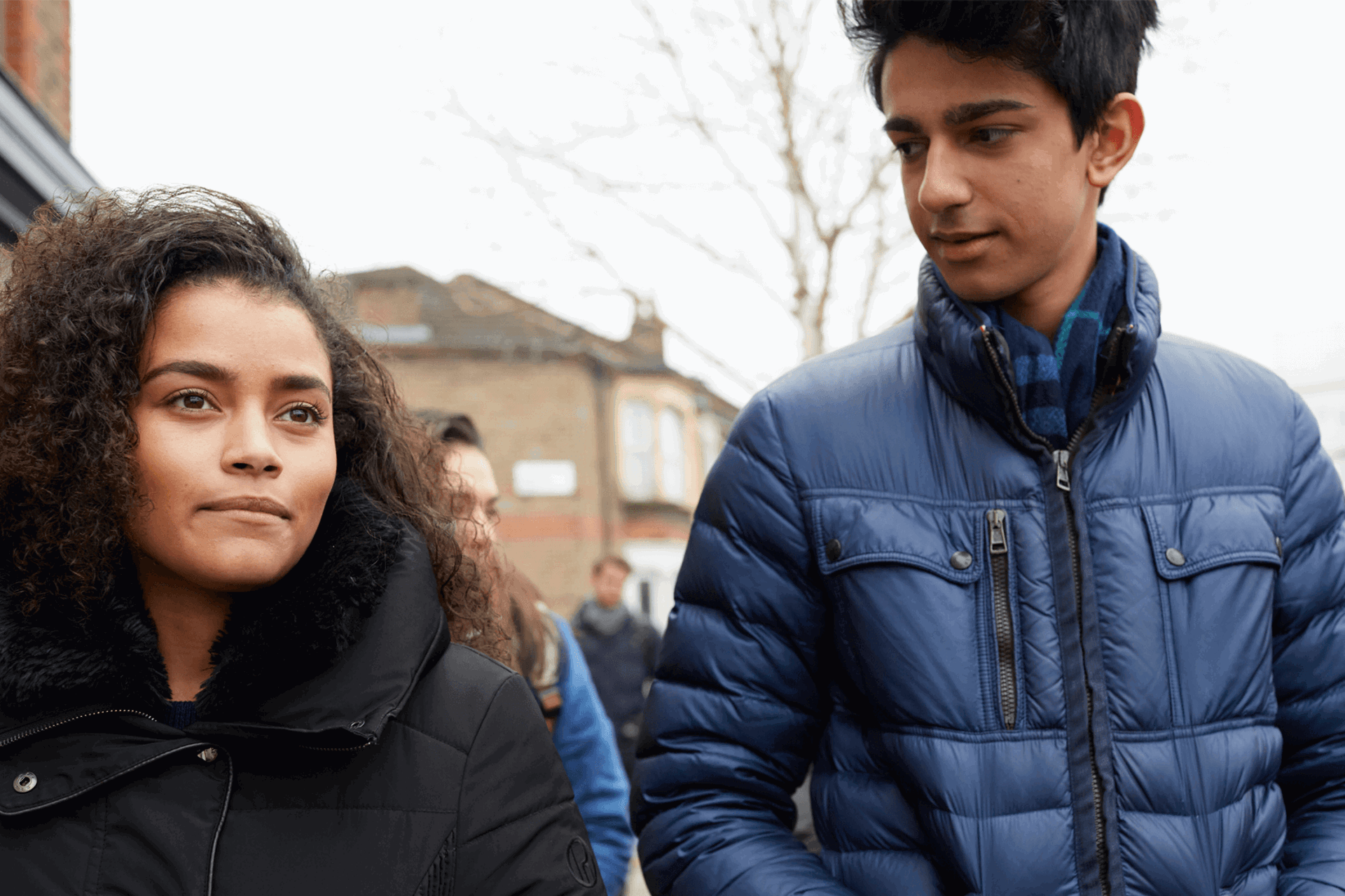 Two young people wearing coats and walking together down a street.