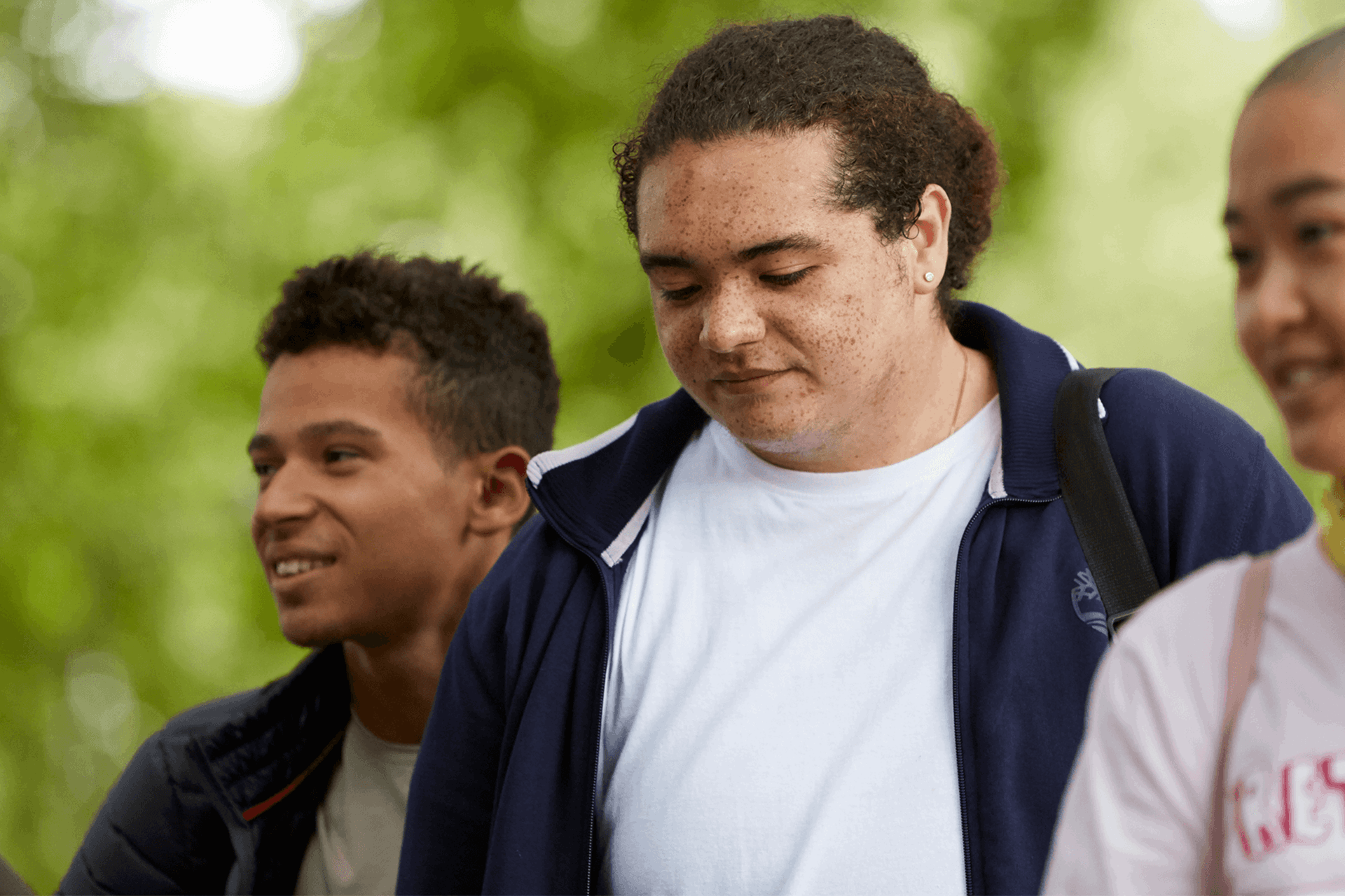 Three young people walk through the woods while talking and smiling together.