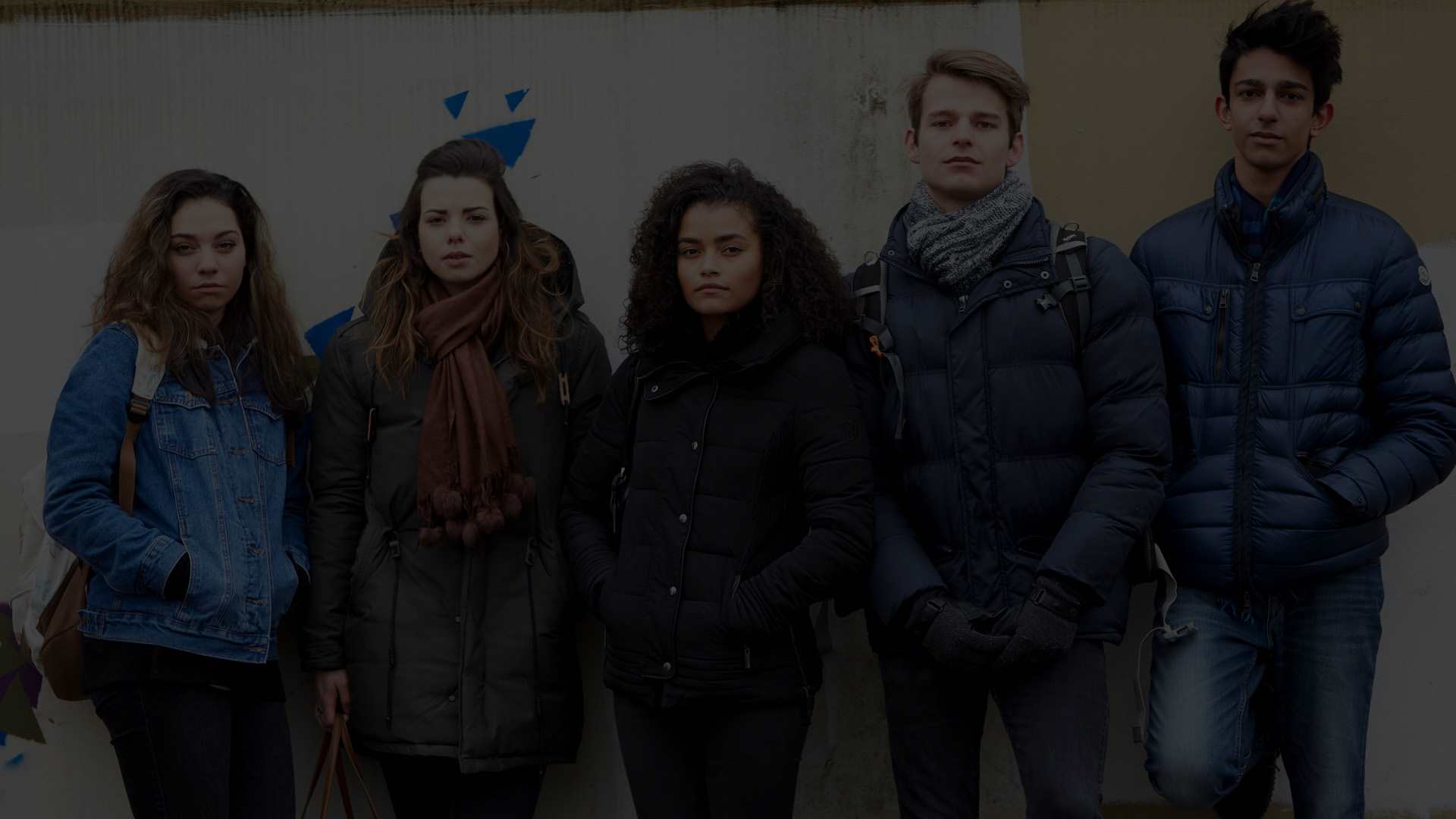 Five young people standing against a brick wall
