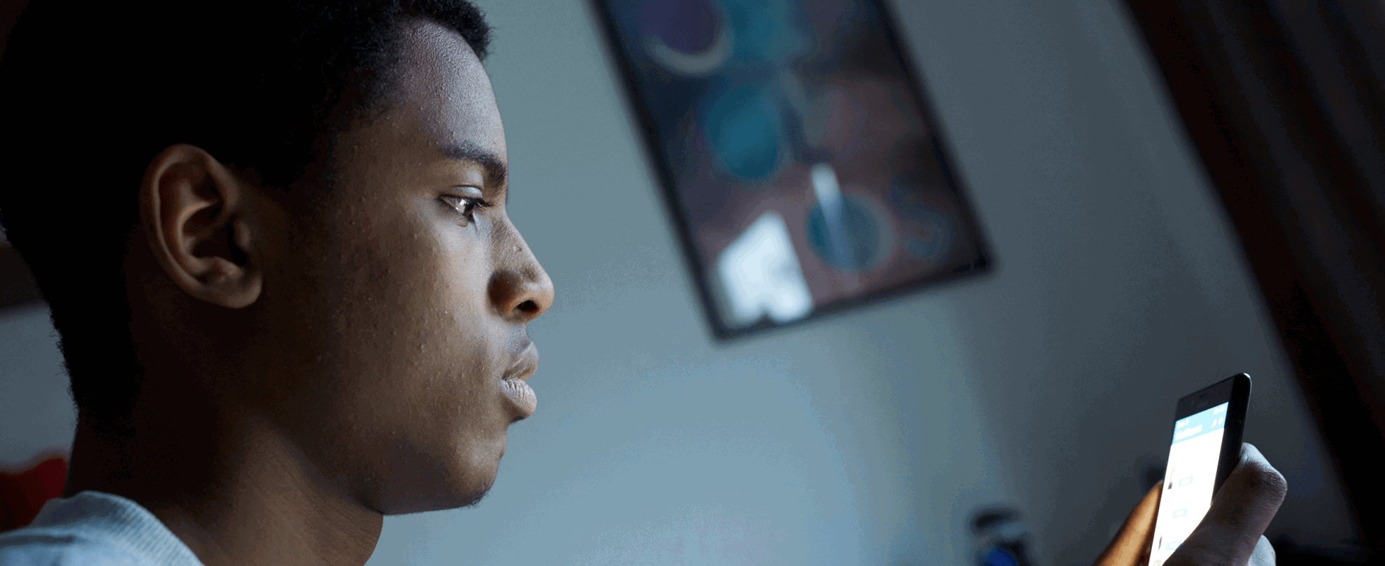 A young person in their bedroom looking at their phone.