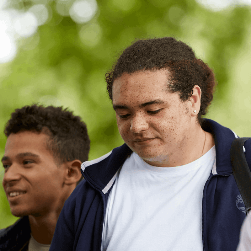 Three young people walking together through a park. Two of them are smiling while a boy in the centre looks worried.